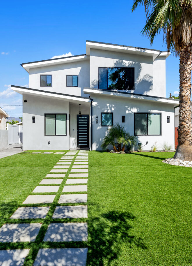 Custom modern new construction home with mid-century-inspired rooflines, dove gray stucco exterior, and black window framing.