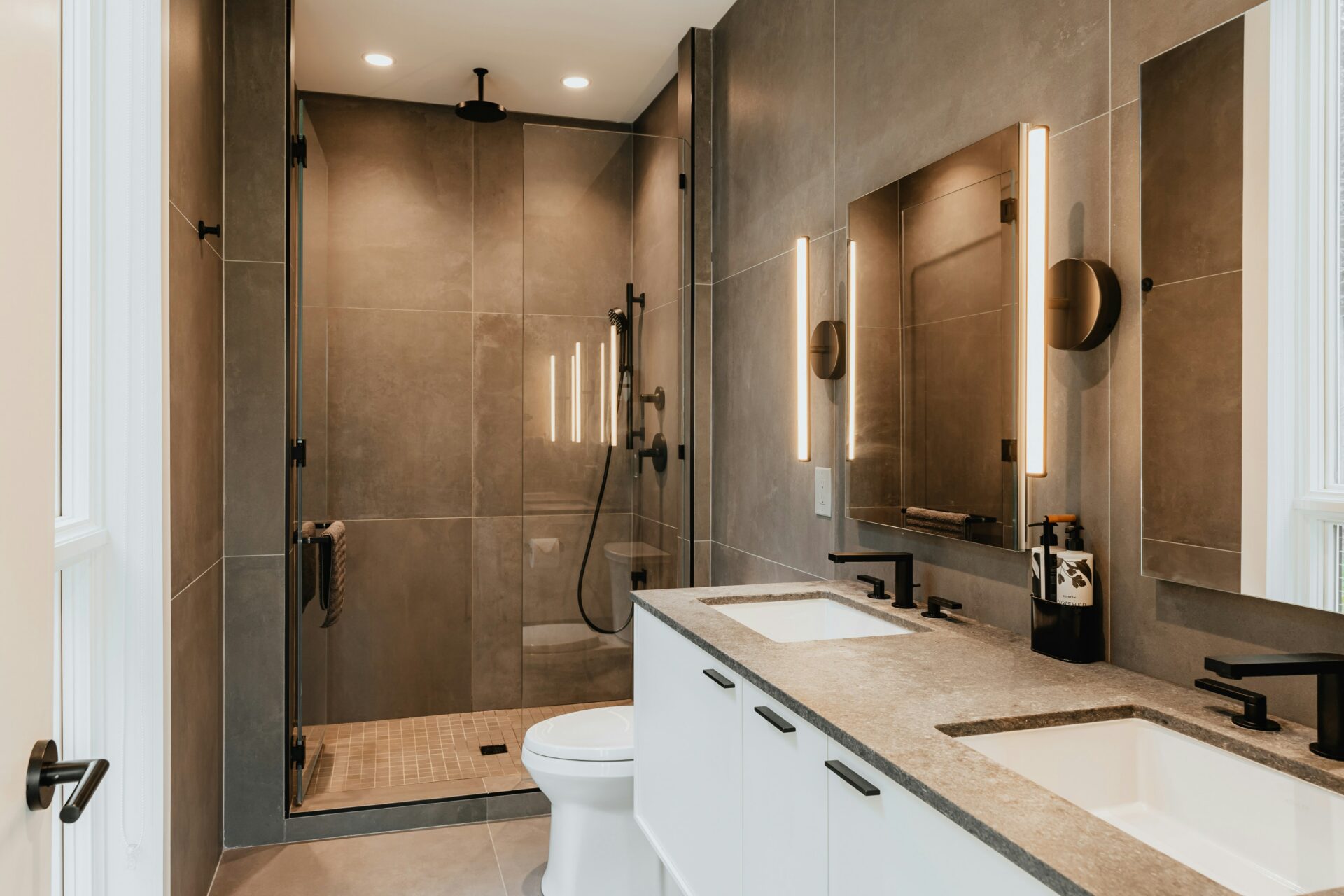 A bathroom with brown tiled walls and a double sink